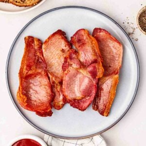 A white plate filled with four rashers of back bacon that have been cooked in an air fryer.