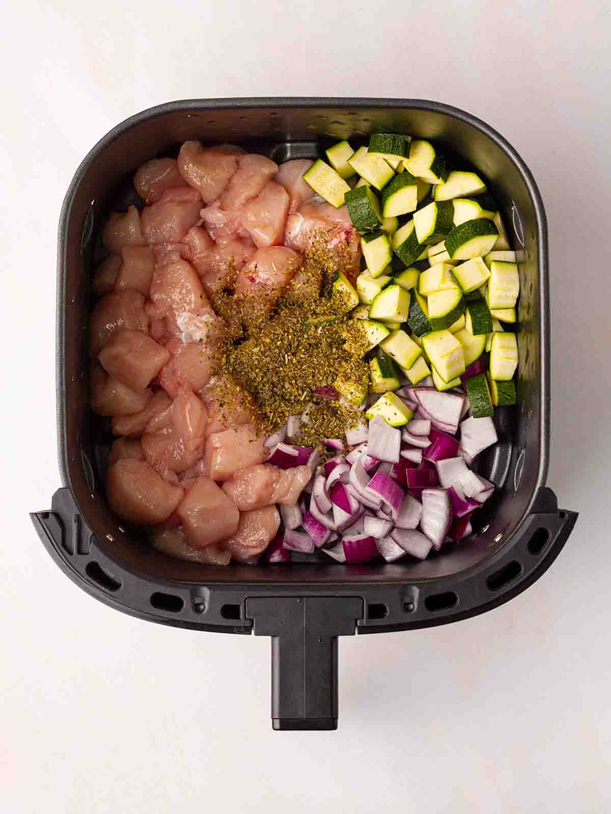 The raw ingredients for Greek Chicken Traybake inside an air fryer for step 1 in the recipe.