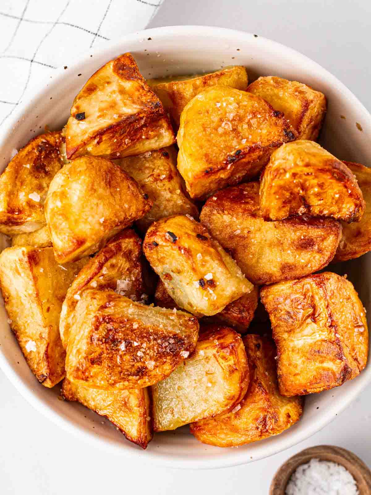 A bowl filled with roast potatoes and a white counter.