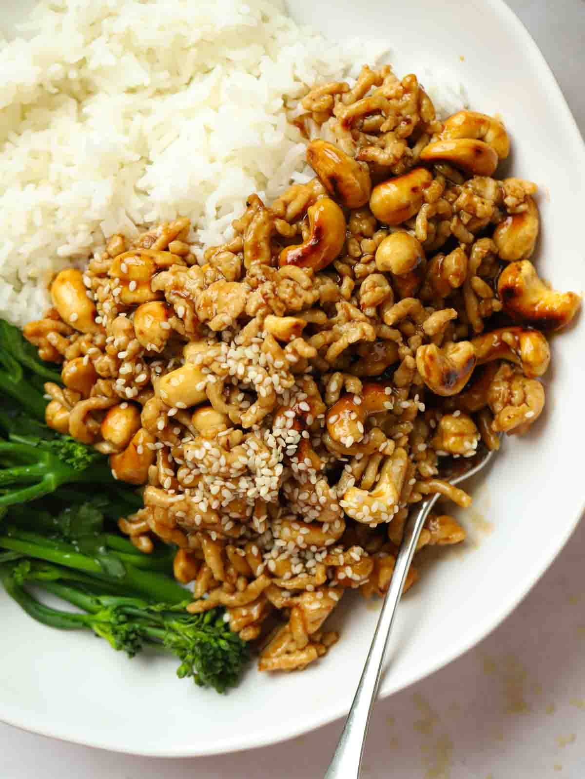 A close look at a cashew chicken mince stir fry, on a plate with rice and broccoli, and a fork sticking out.