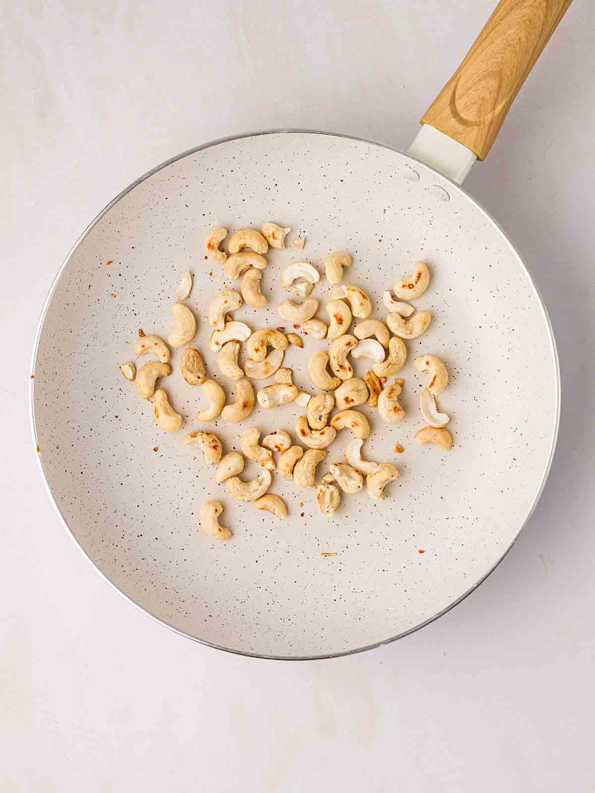 Cashews being toasted in a white pan.