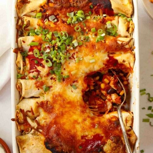 A spoon sticking in a dish with cooked Chicken Enchiladas.