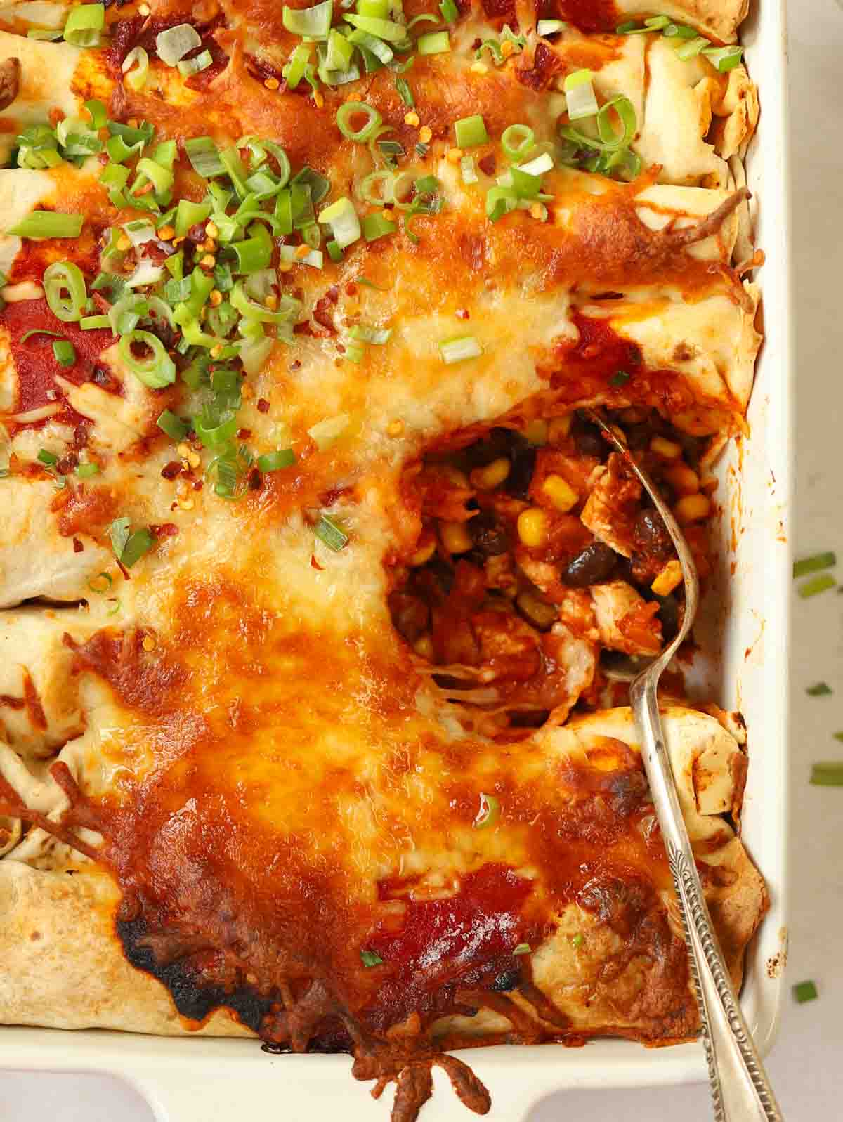A spoon in a dish with cooked Chicken Enchiladas, serving up ready for dinner.