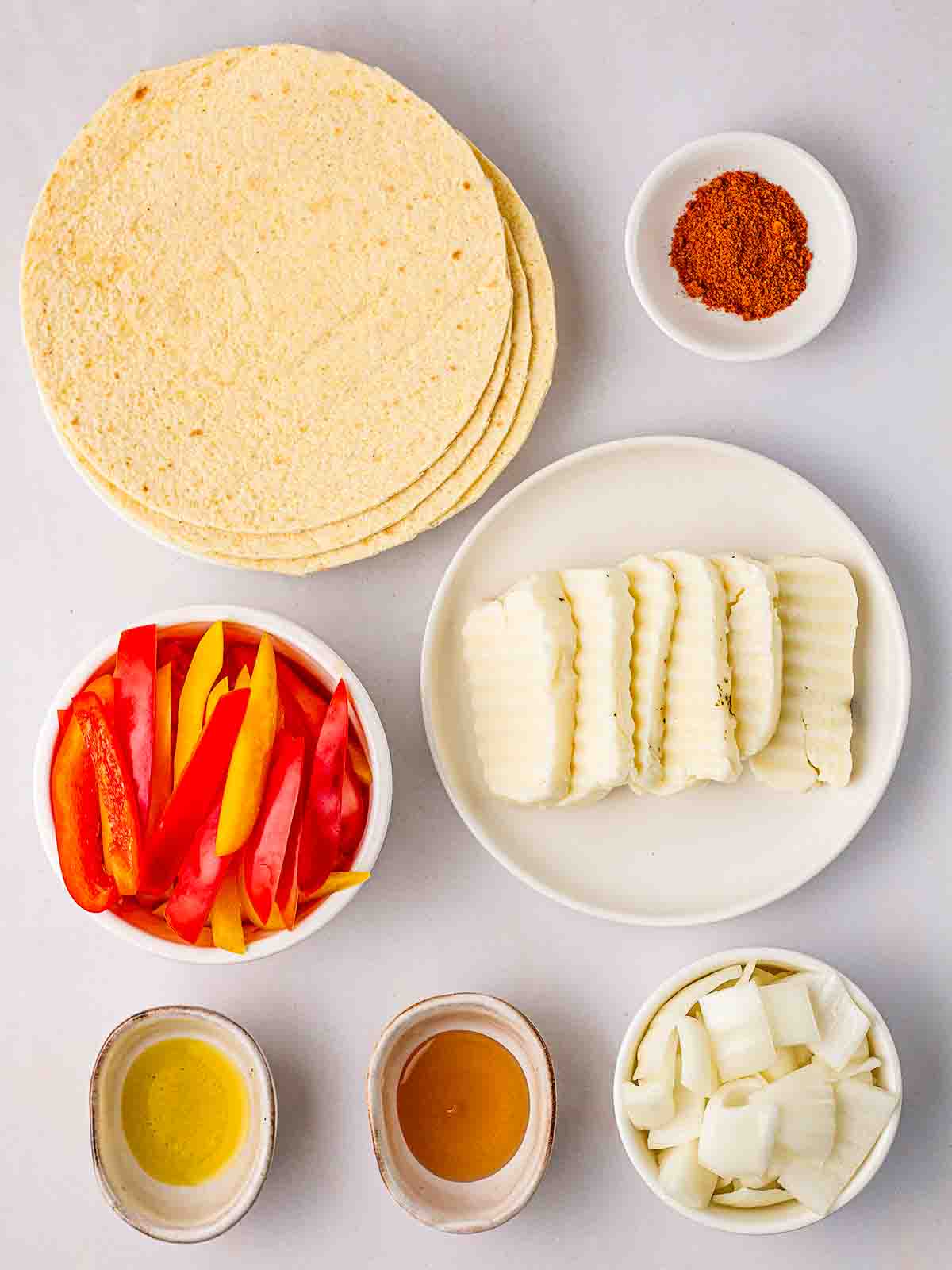 The ingredients for halloumi fajitas laid out in plates and bowls on a white counter top.