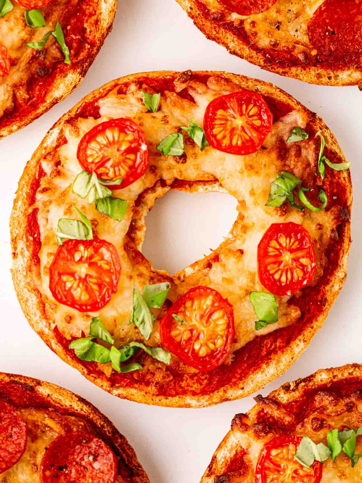 A close up of a pizza bagel with tomato and basil on top.