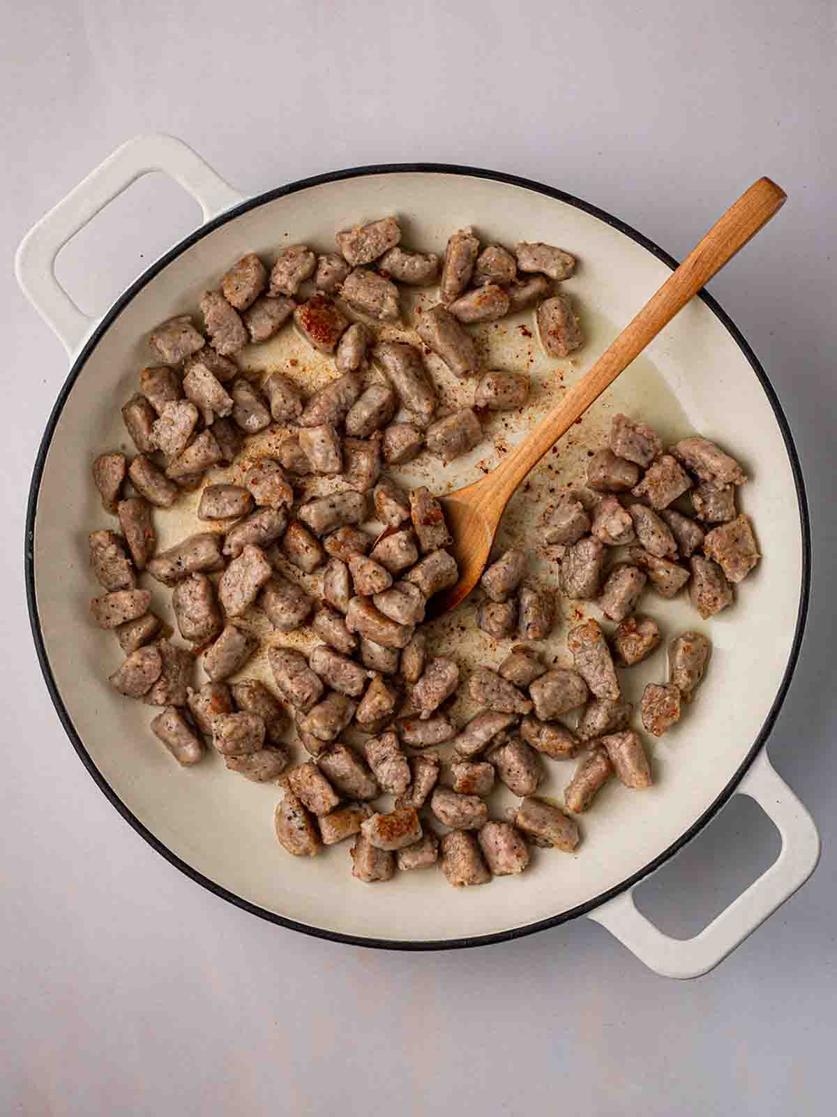 A pan filled with chunks of sausage, browning in oil.