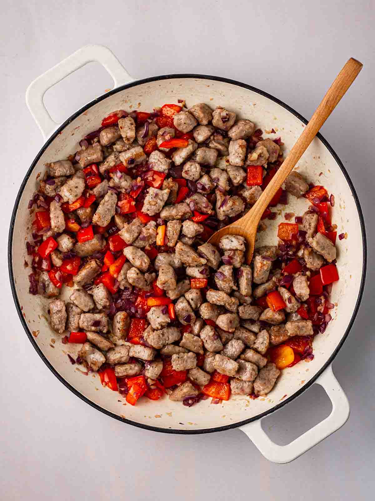 Chucks of cooked sausage with red pepper cooking in a pan.