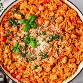 A close look at one pot sausage orzo pasta dish in pan with basil and parmesan on top.