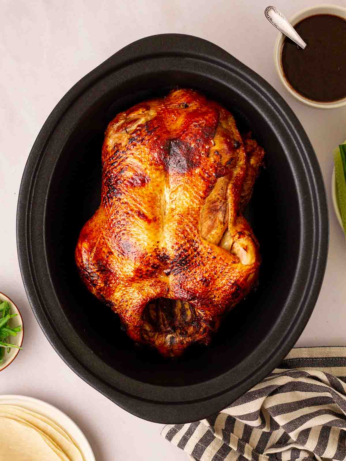 A slow cooker with a browned duck inside for Peking Style Duck recipe. A bowl of sauce to the side.