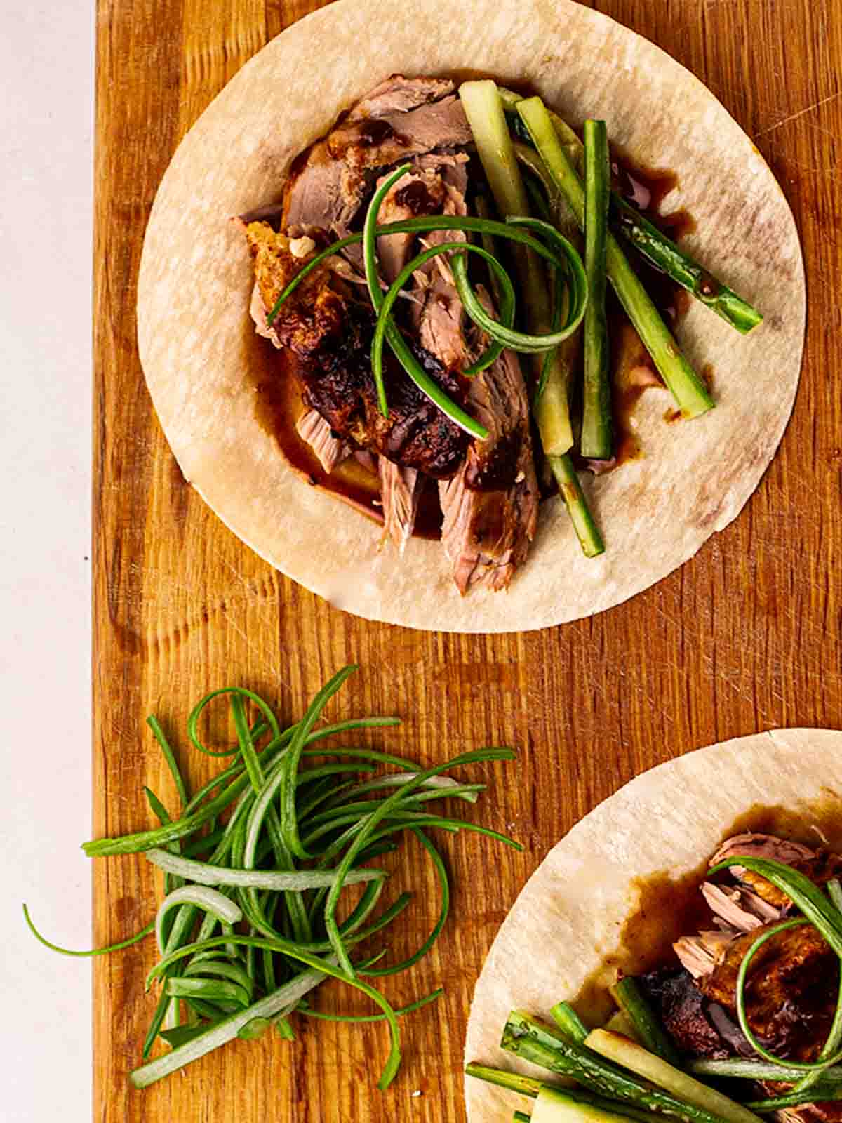 A wooden board with Chinese pancakes filled with Peking style duck, cucumber, onions and sauce.