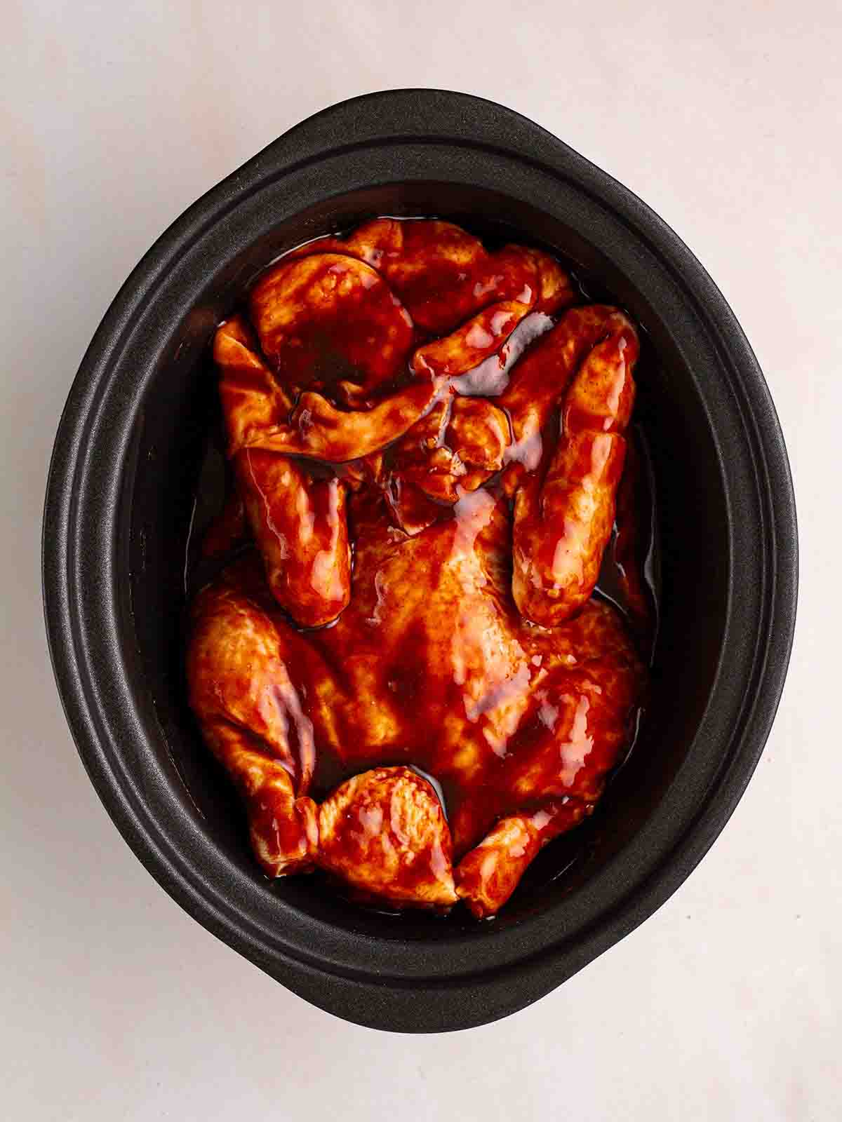 A sauce coated duck upside down in a slow cooker, ready to be cooked.