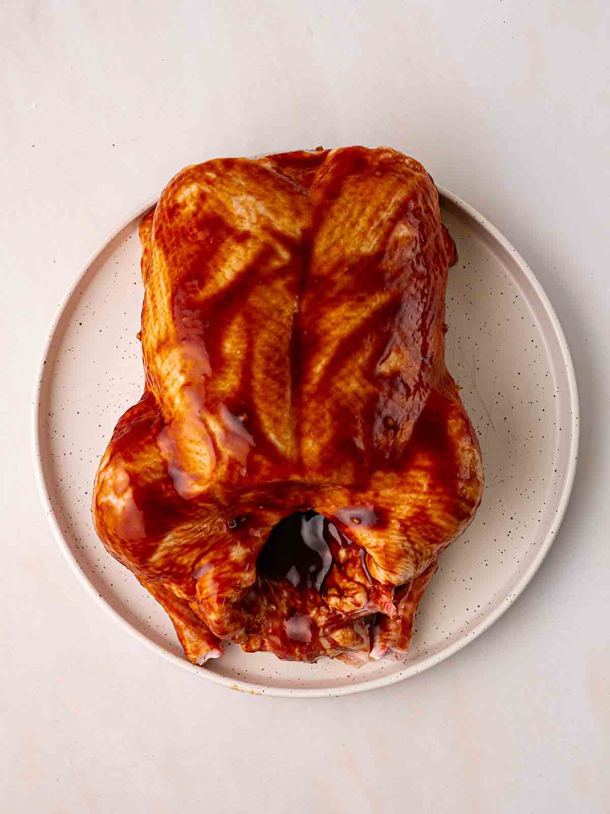A plate with a raw duck, coated in peking sauce, ready to be cooked.