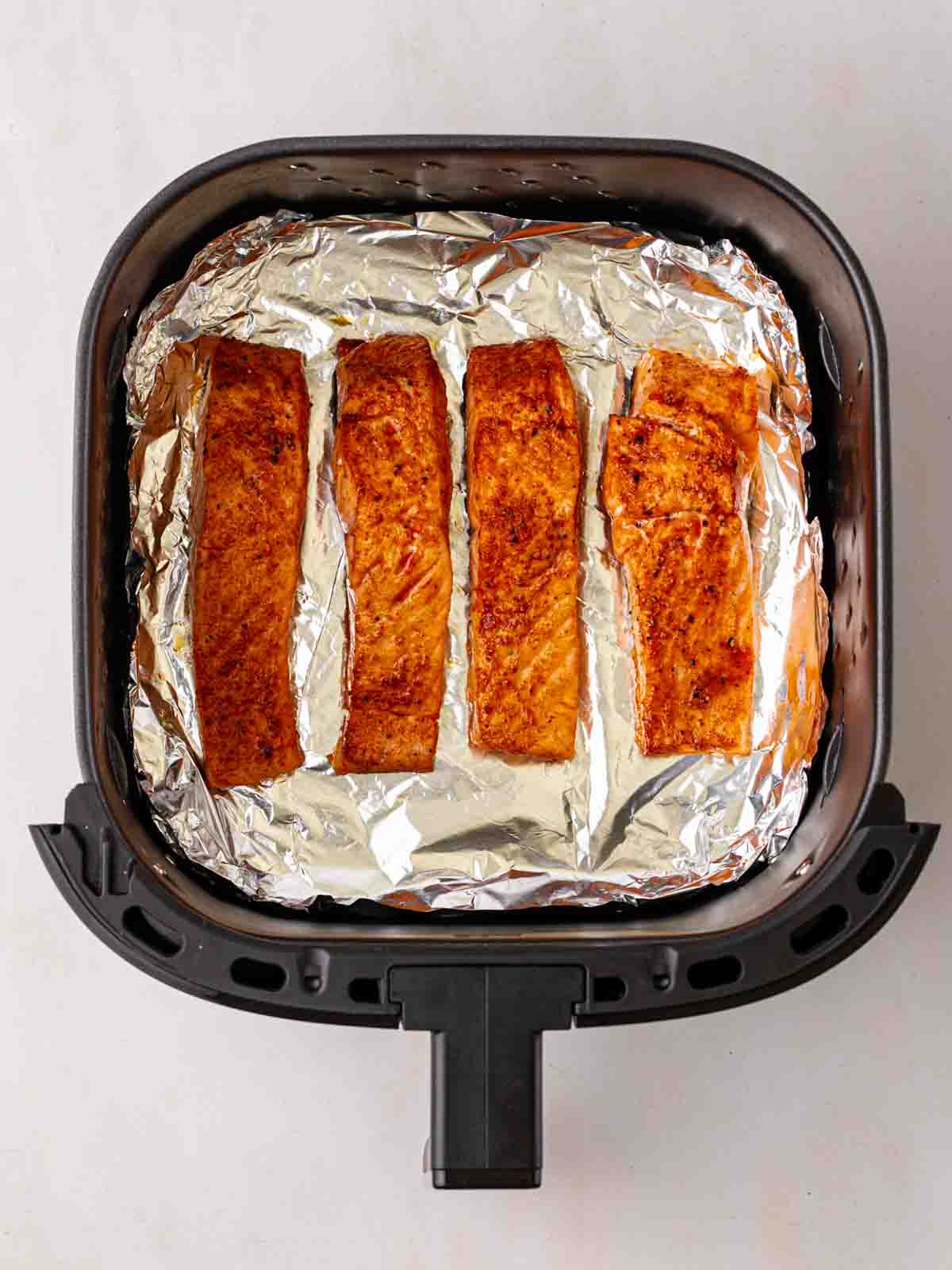 Four cooked salmon fillets in an air fryer on top of foil.