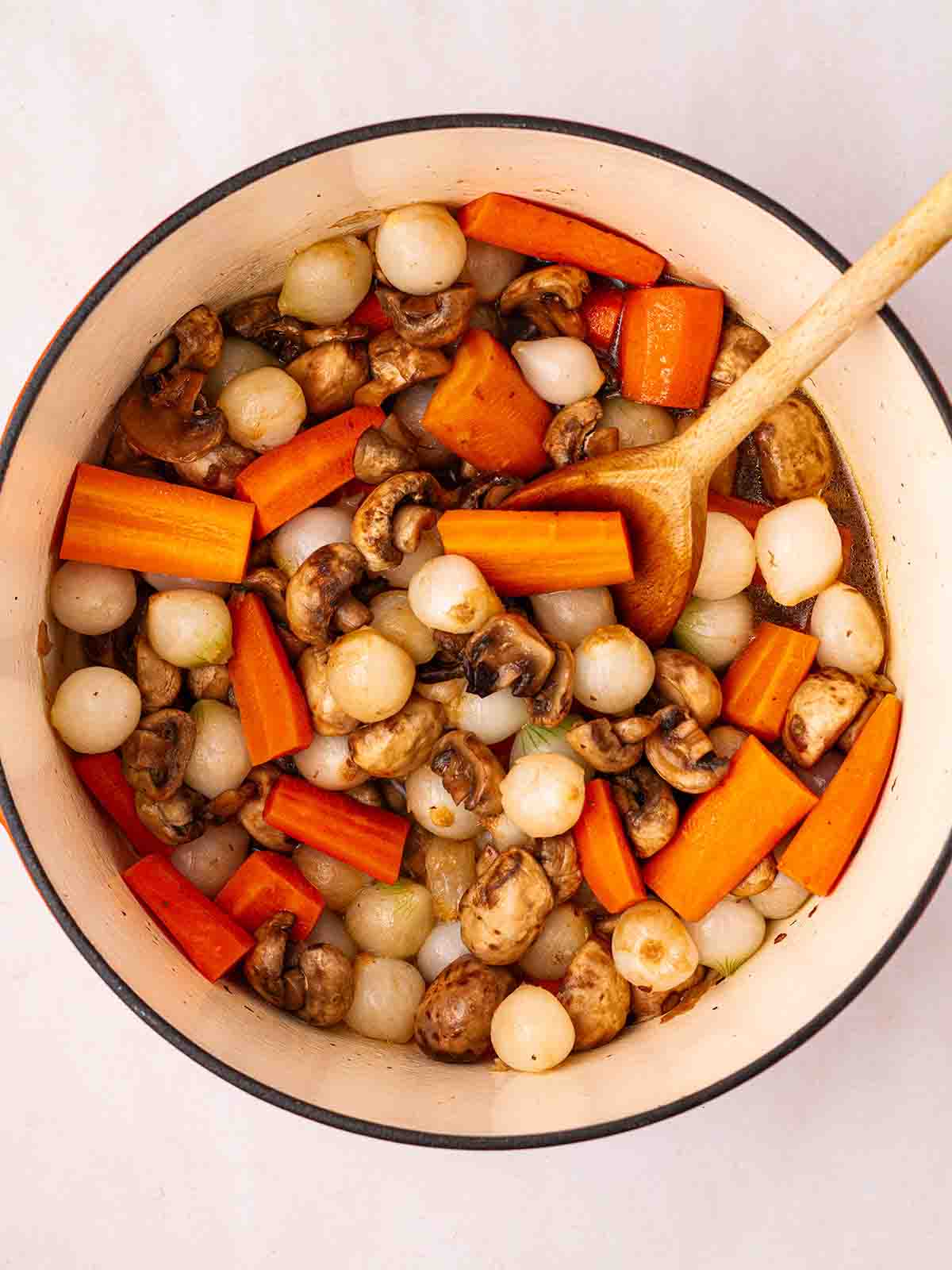 A pan filled with cooking carrots, shallots, mushrooms in a gravy for step 2 in the recipe for beef bourguignon.