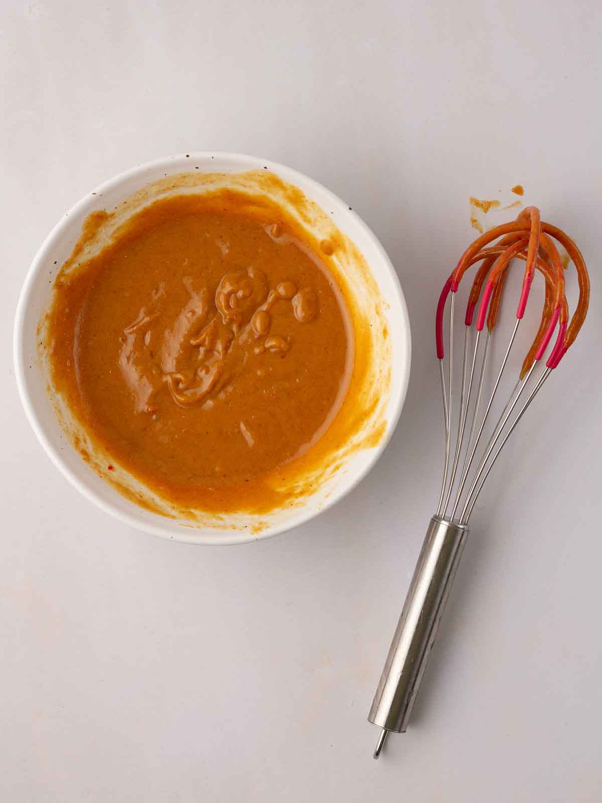 Peanut butter dressing in a bowl with a whisk to the side for step 4 in the recipe for Cabbage Salad.
