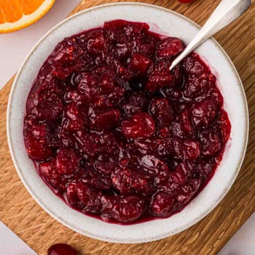 A bowl of cranberry sauce on a wooden board, with ingredients around the edges.
