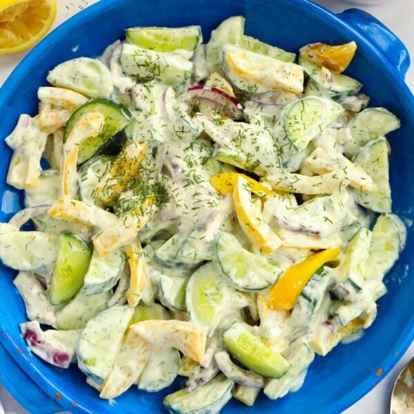 A blue salad bowl filled with cucumber salad with yoghurt dressing.