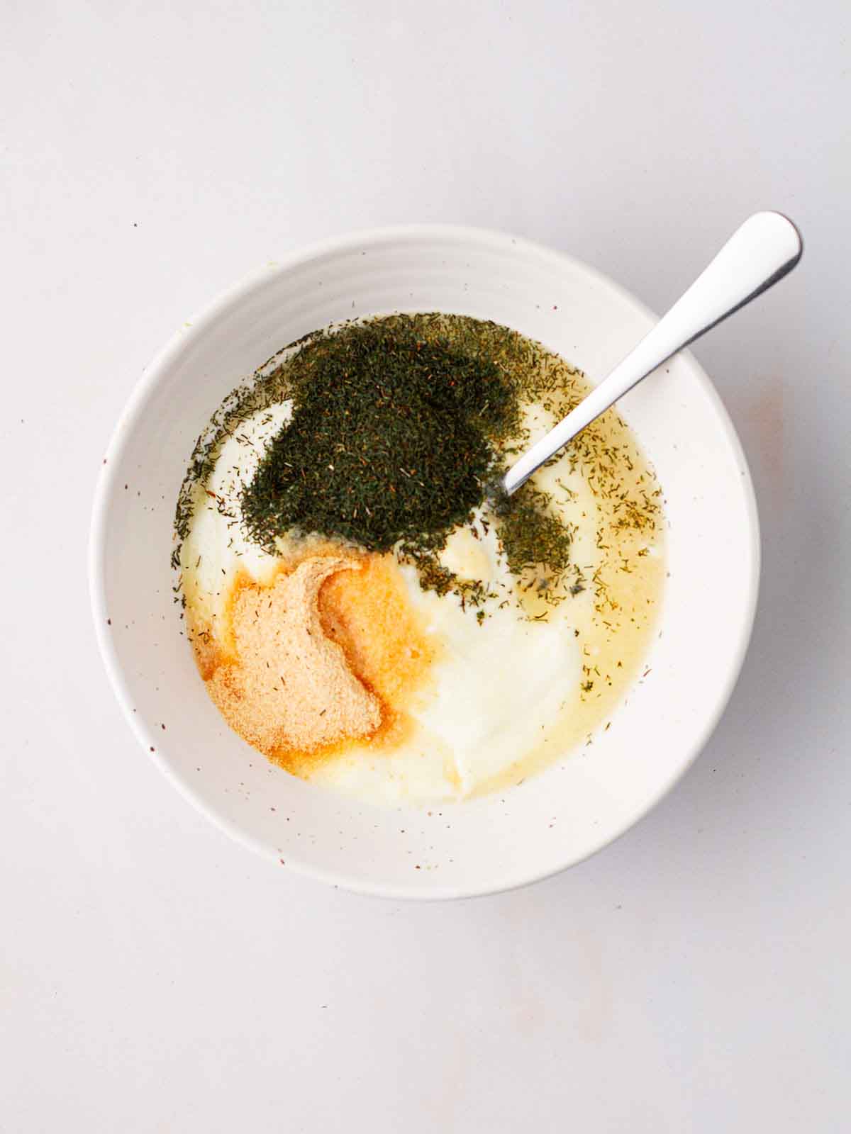 A bowl of salad dressing before being mixed, including yoghurt, garlic powder, dill and lemon juice.