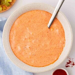 An orange sauce in a white bowl with spoon sticking out for a homemade Big Mac Sauce recipe.