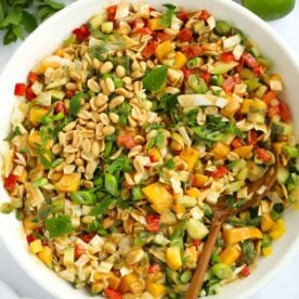 A white bowl filled with Cabbage Salad ingredients, including mango, peanuts, spring onion and cucumber.