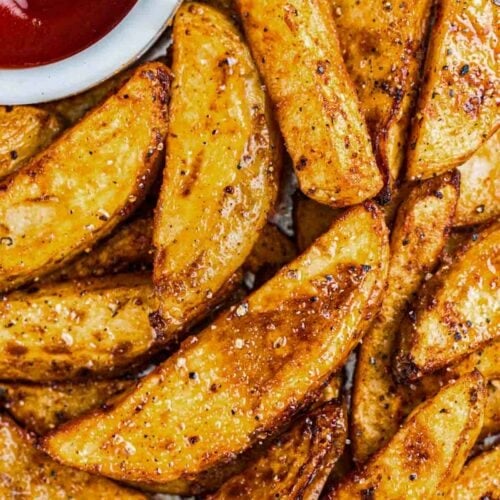 A plate of potato wedges with a side of ketchup to dip.