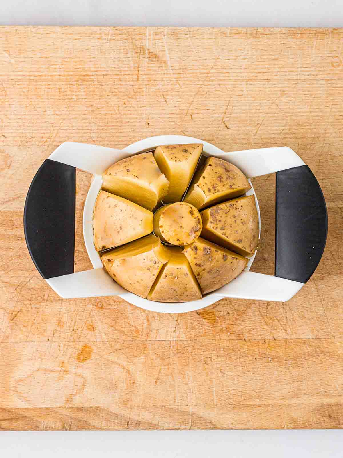 A potato being cut into wedges on a chopping board by an apple divider.
