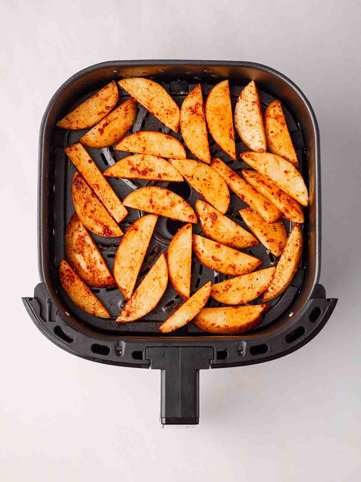 An air fryer tray filled with seasoned potato wedges.