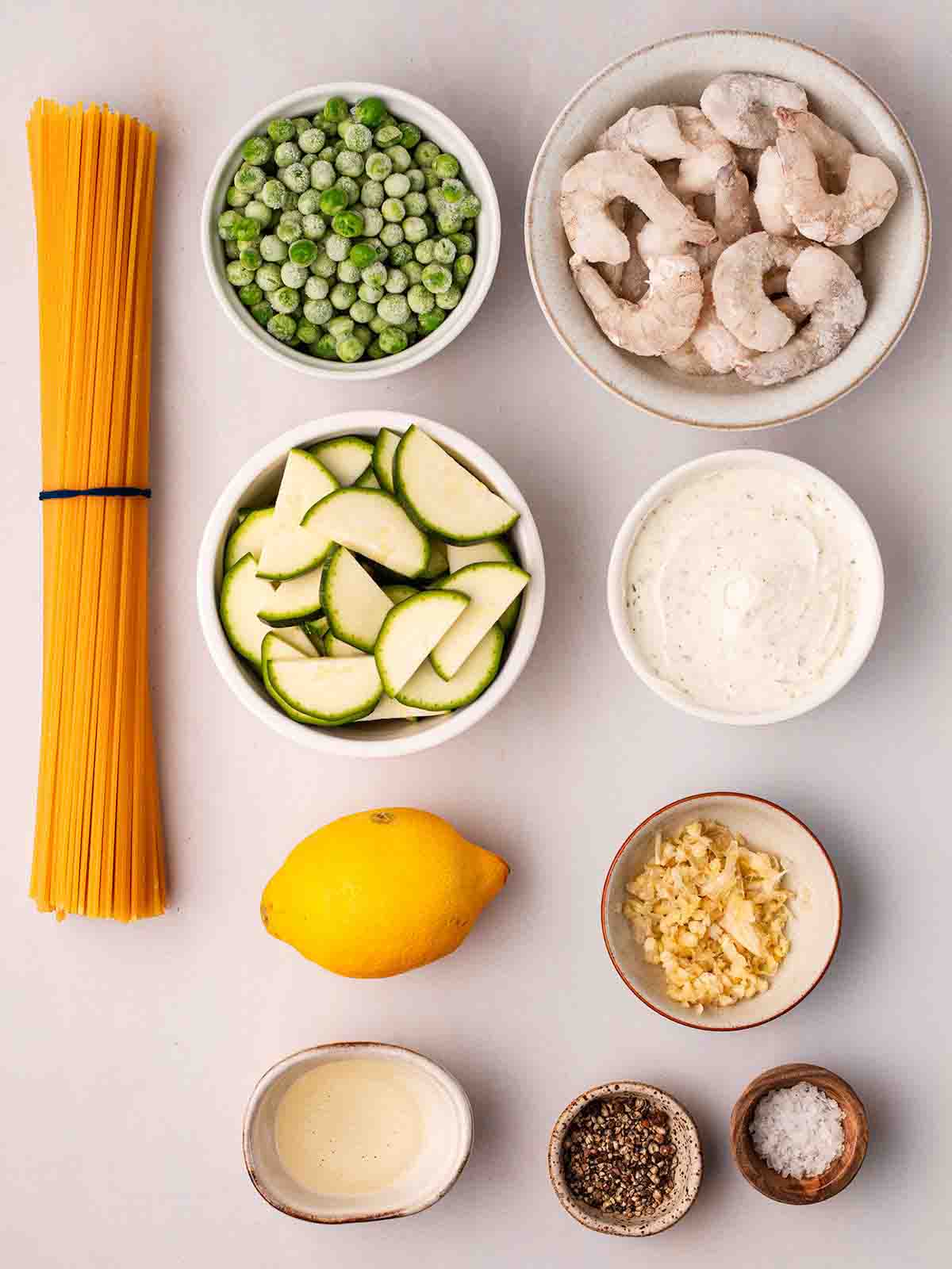 The ingredients for making prawn pasta recipe on a white counter top in small bowls.