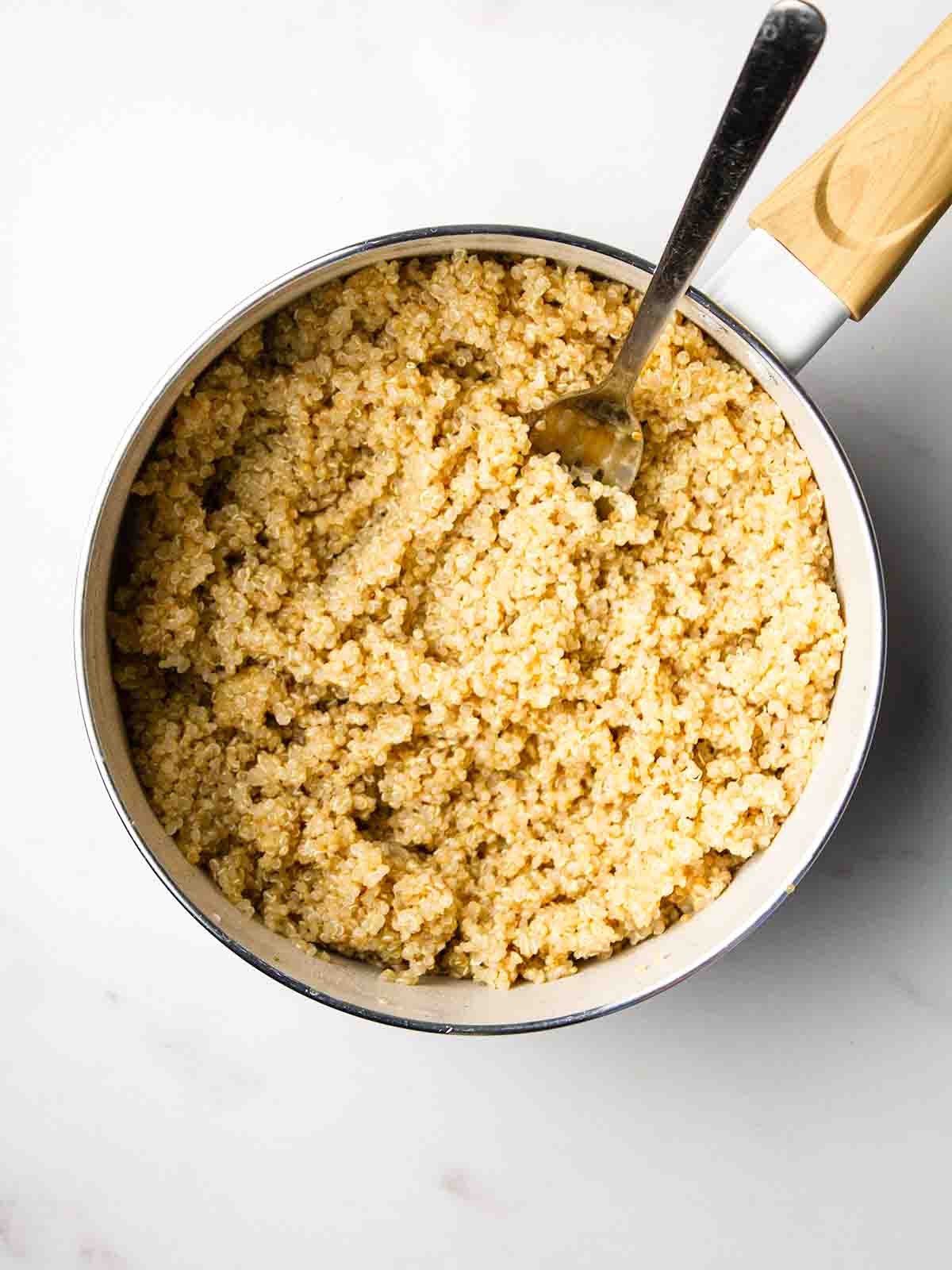 A pan with fluffed up cooked quinoa with a fork for step 4 in the recipe for Quinoa Salad.
