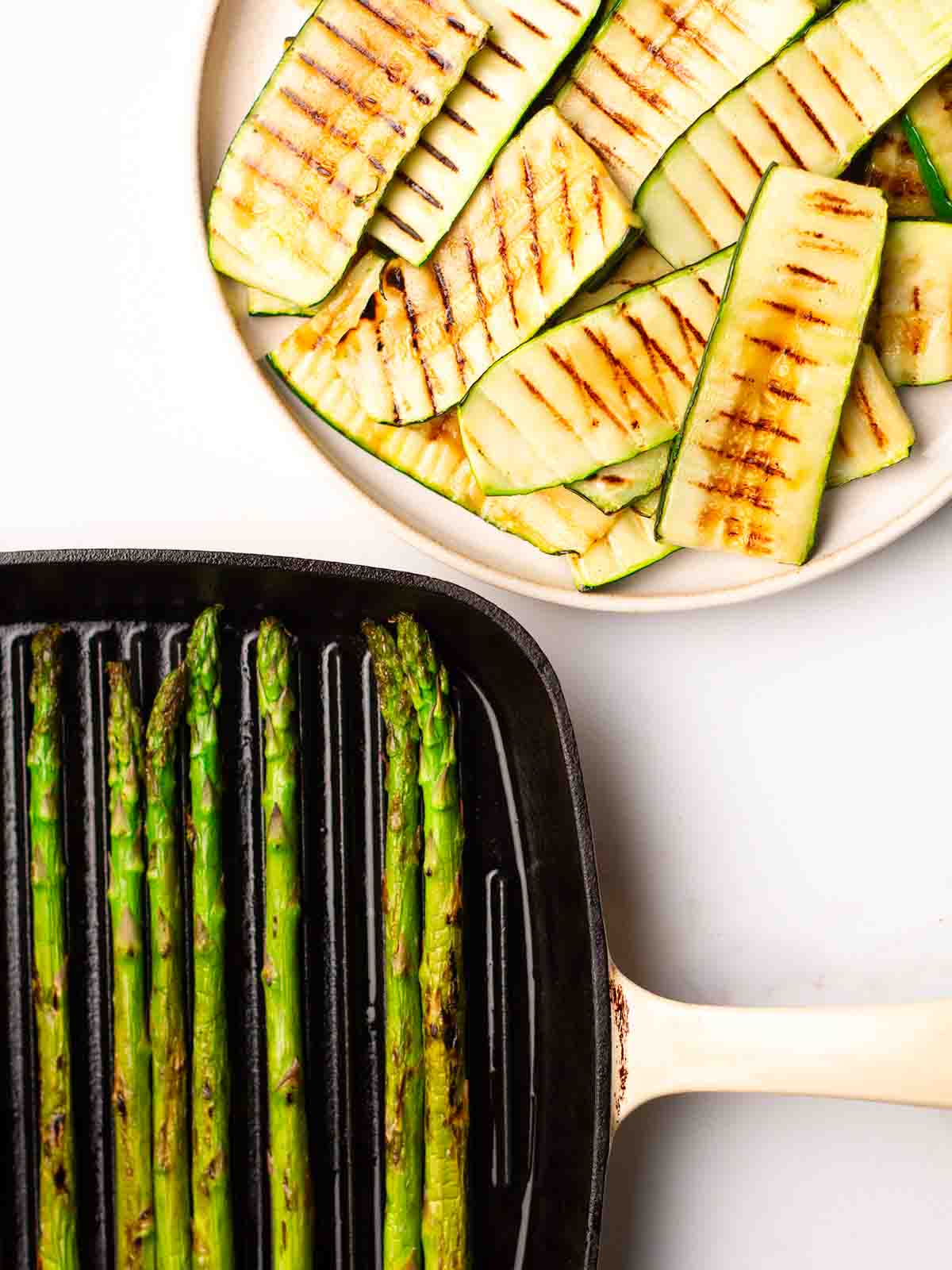 A plate of grilled sliced courgettes and a pan filled with grilled asparagus for step 2 in the recipe for Quinoa Salad.