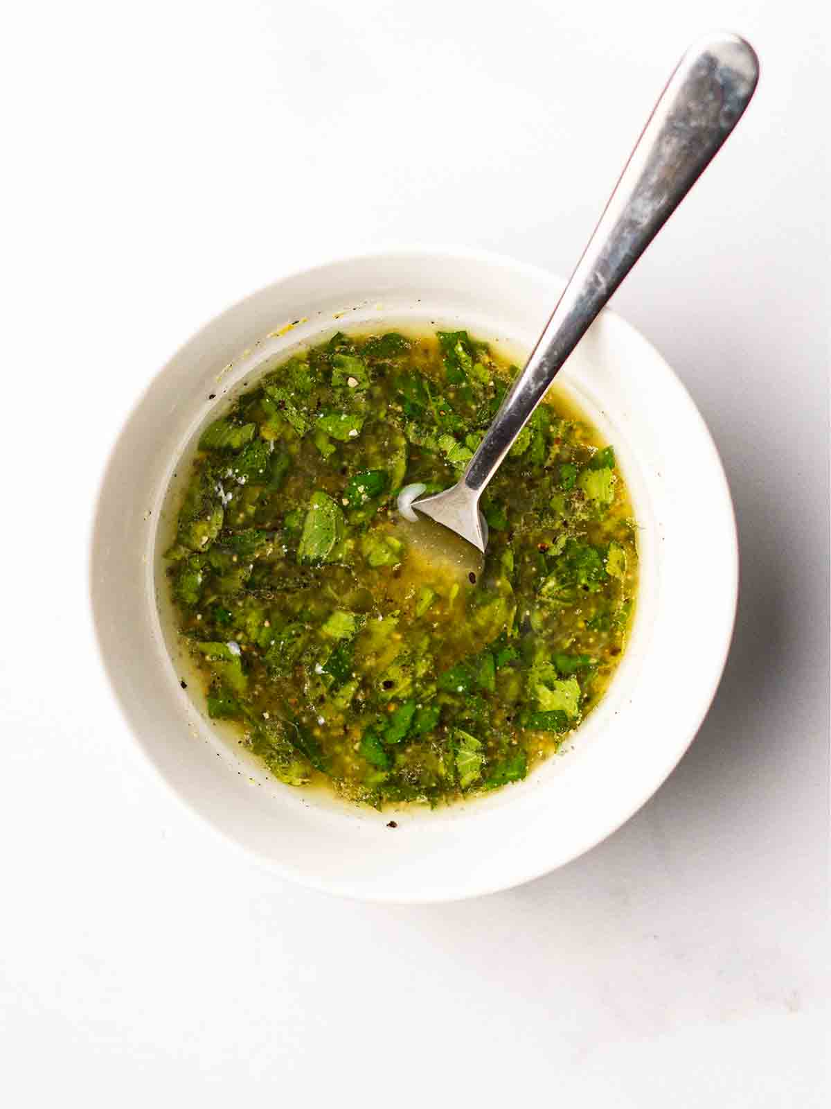 A homemade dressing in a white bowl with a fork for the recipe Quinoa Salad.