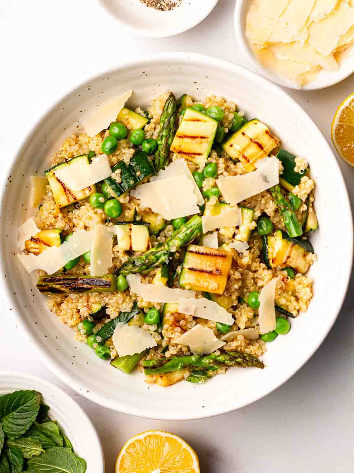 A white bowl filled with Quinoa Salad, including courgettes, asparagus and peas.