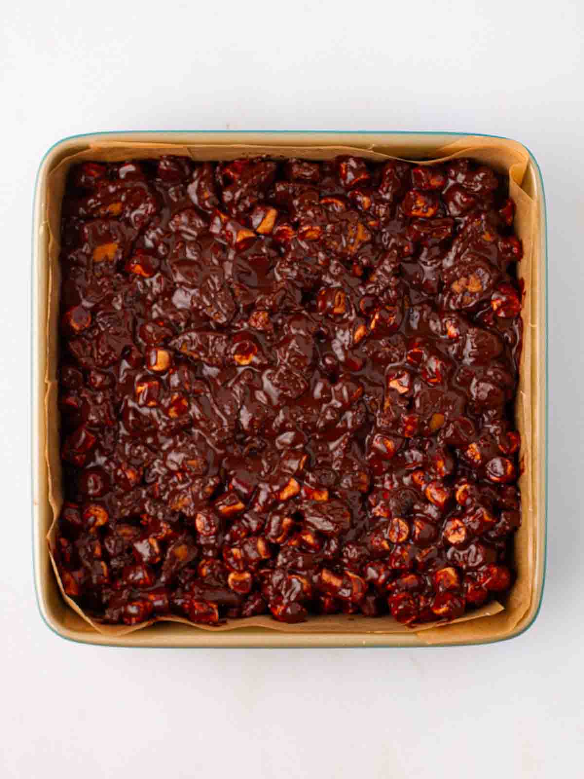 A square tray mixed with chocolate, marshmallow and biscuit for step 4 in the recipe for Rocky Road.