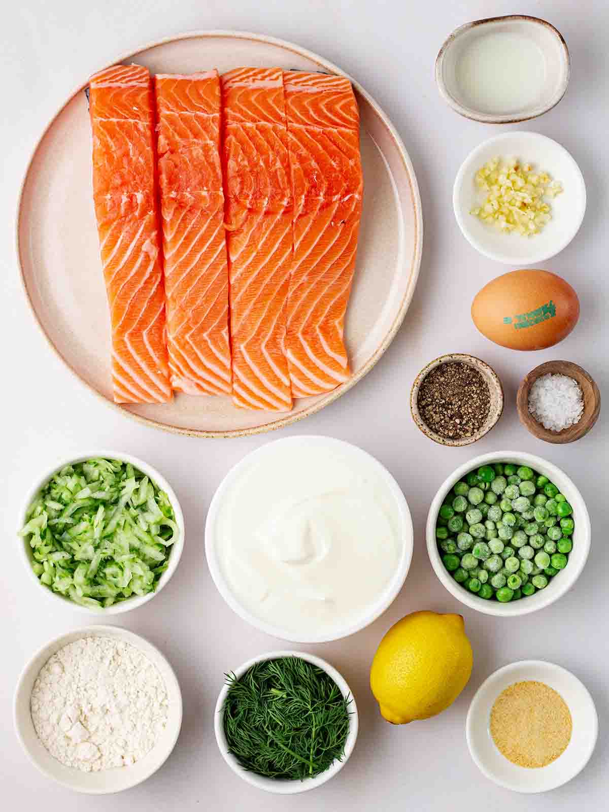 The ingredients for salmon burgers laid out on a counter top in plates and small bowls.