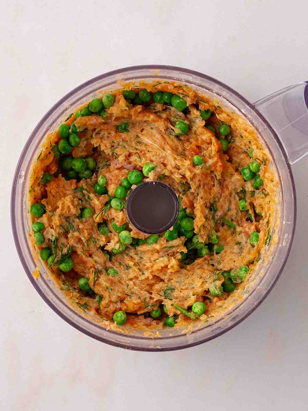 A blender with the mixture for Salmon Burgers inside with peas about to be stirred in.