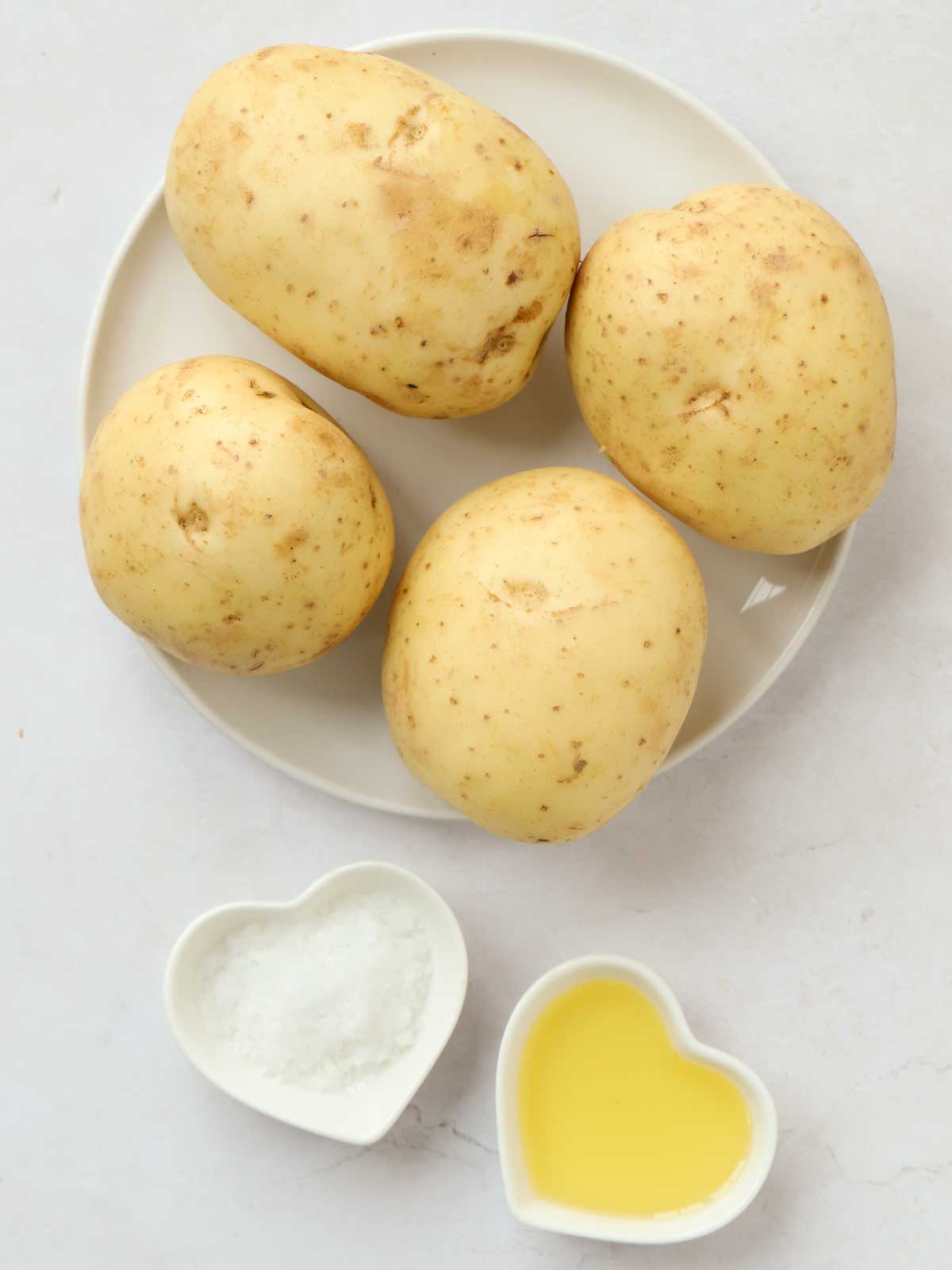 The ingredients for baked potatoes on a white counter. Potatoes, salt and oil.