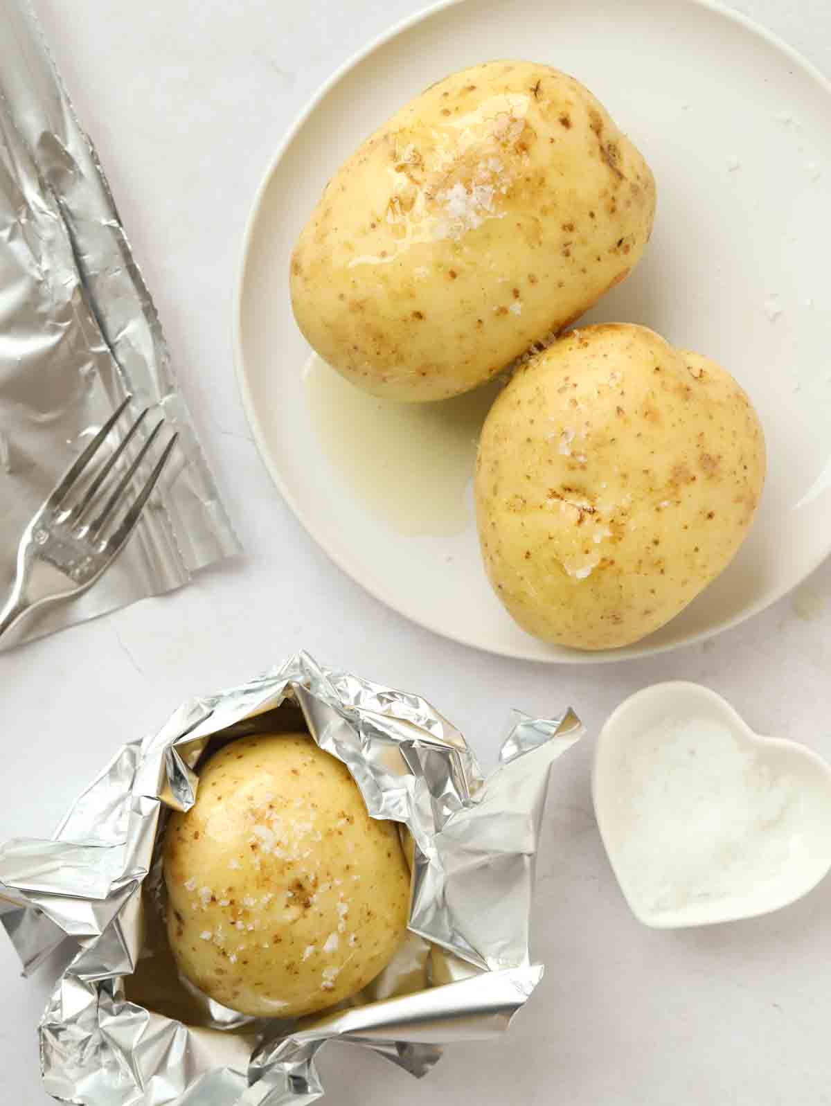 Three baked potatoes with salt and about to be wrapped in foil for Slow Cooker Jacket Potatoes recipe.