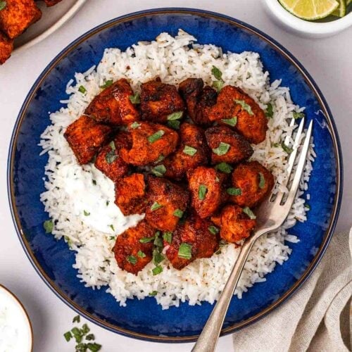 Cooked tandoori chicken and rice on a blue plate with a fork, surrounded by smaller pots.