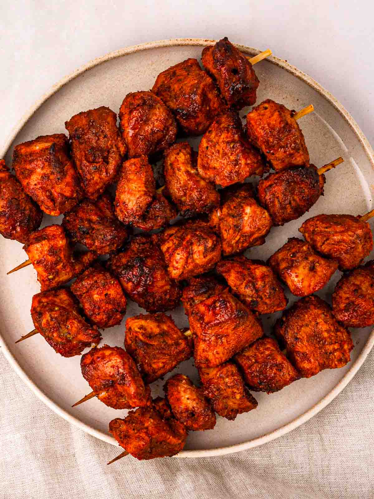 Cooked chunks of Tandoori Chicken on wooden skewers, on a plate.