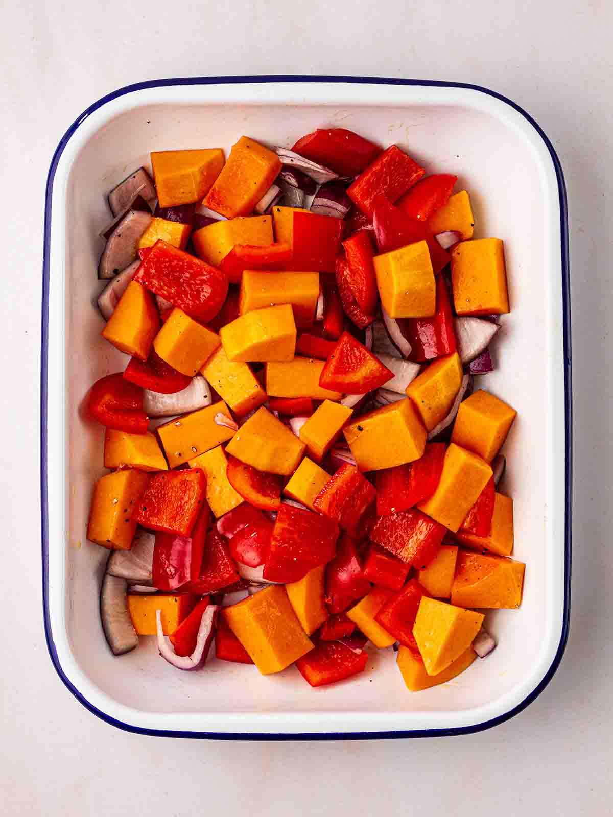 Chopped up butternut squash, onion and peppers in a roasting dish for step 1 of the recipe for Vegetarian Enchiladas.