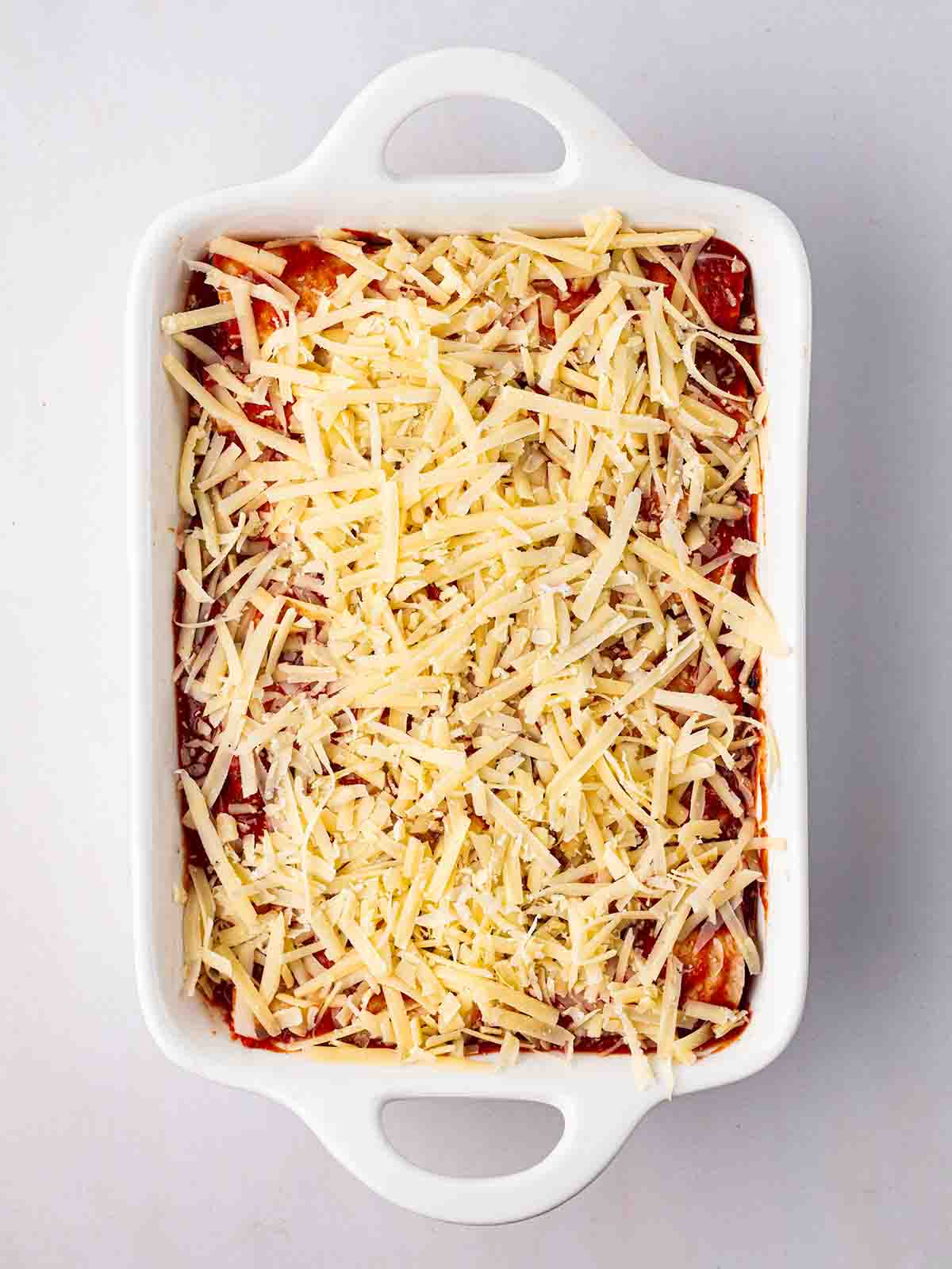 A white oven dish filled with vegetarian enchiladas and topped with grated cheese for for step 6 of the recipe for Vegetarian Enchiladas.