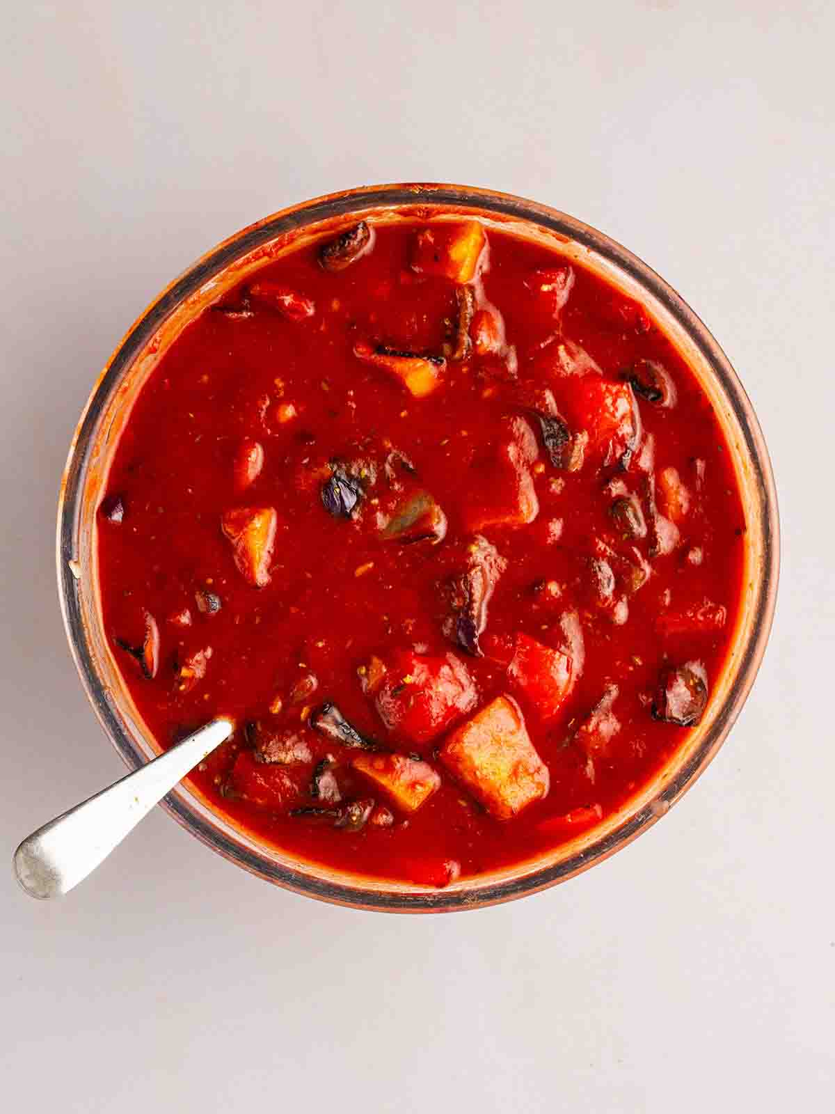 A bowl filled with roasted vegetables and beans in a tomato sauce for step 2 of the recipe for Vegetarian Enchiladas.