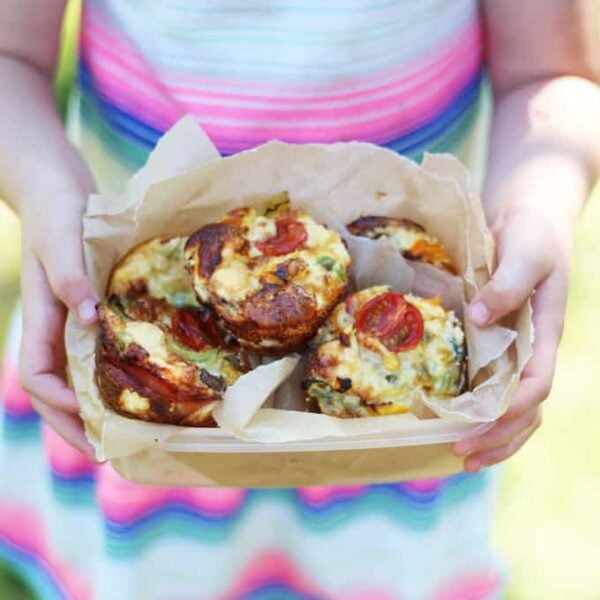 A lunch box filled with mini crustless quiches, held in the hands of a little girl.