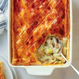 A close up of a chicken and leek pie being dished up from the corner of the dish, showing a crusty golden crust and a creamy chicken filling.