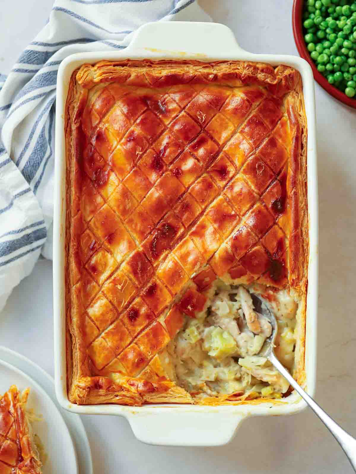 A golden topped chicken and leek pie, straight out of the oven, with a portion missing from the corner, being spooned out.