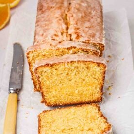 A loaf Orange Drizzle Cake ready baked, partially sliced, with a knife to the side, ready to eat.