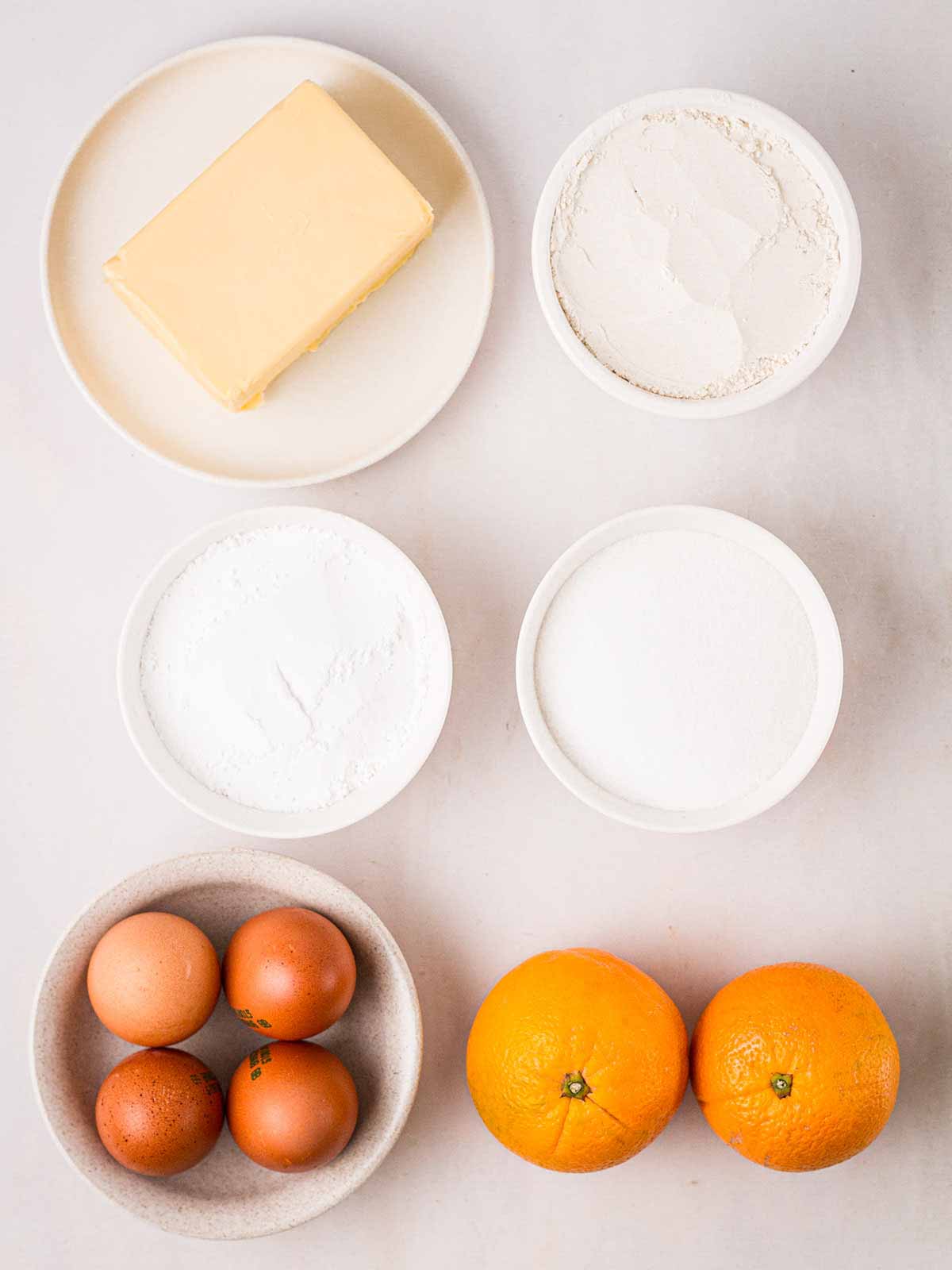 The ingredients for an Orange Drizzle Cake in bowls on a white counter.
