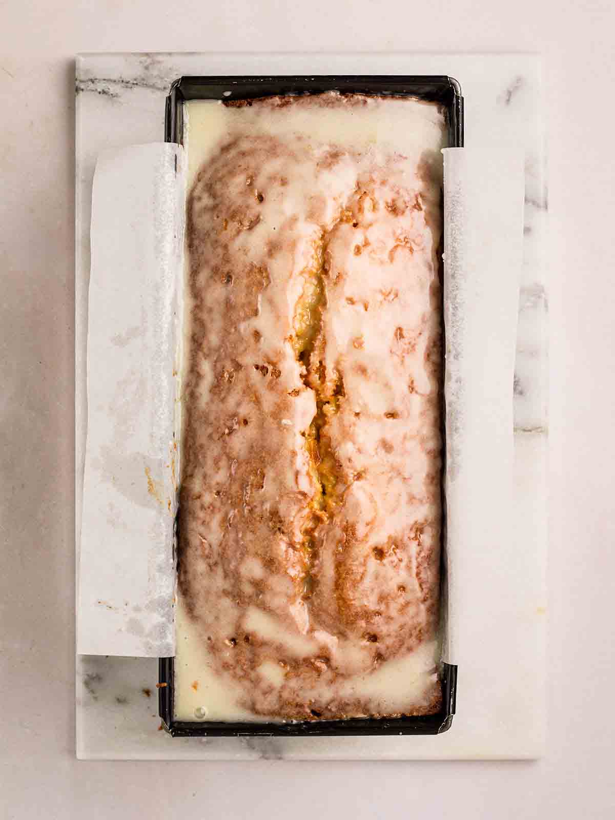 A loaf tin filled with Orange Drizzle Cake, topped with icing.