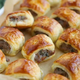 Rows of freshly made sausage rolls on a baking tray.