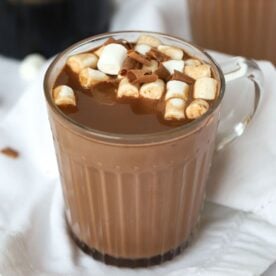 A mug filled with boozy Baileys Hot Chocolate, made in the slow cooker, on a table, topped with marshmallows, ready to eat.
